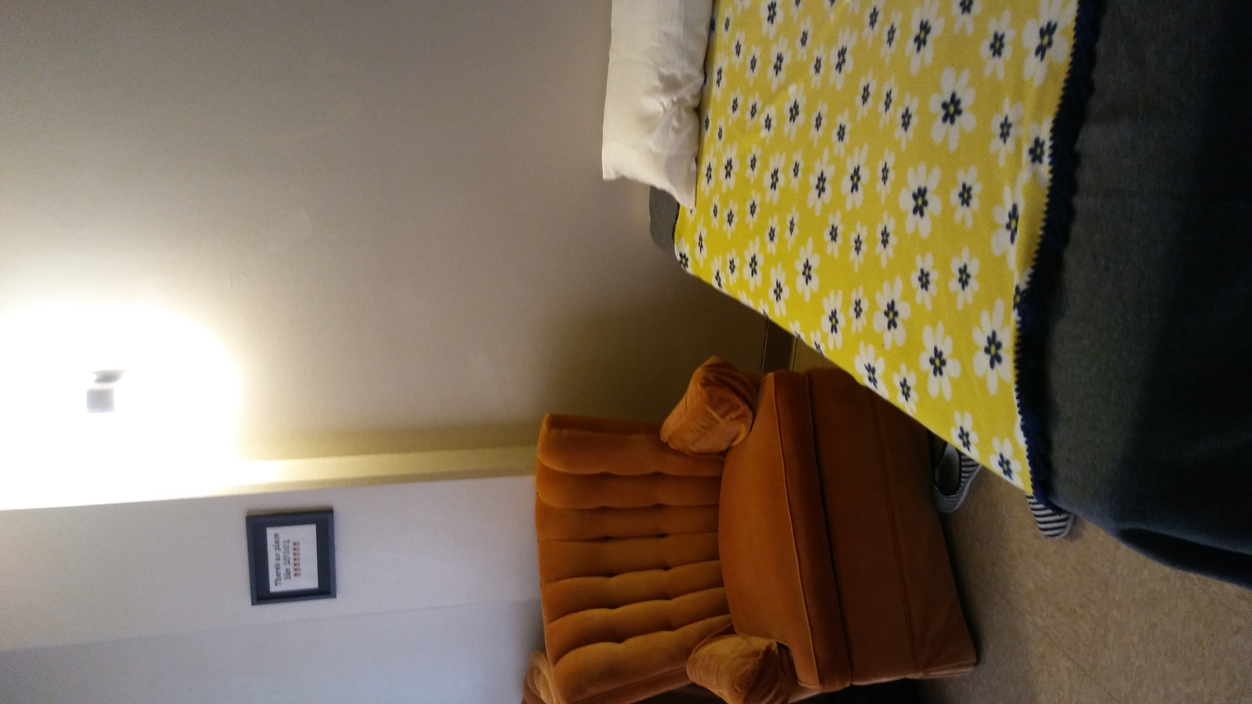 a twin bed with two blankets and one pillow with an old orange armchair next to it